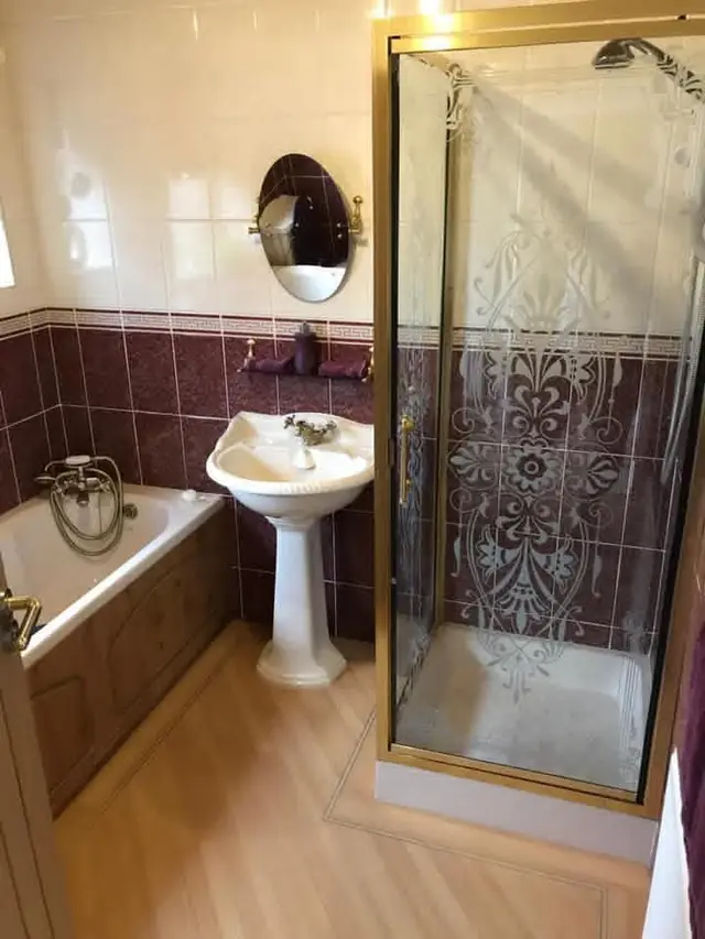 The bathroom before: a fitted bath, a pedestal basin and a shower cubicle, with purple border tiles.