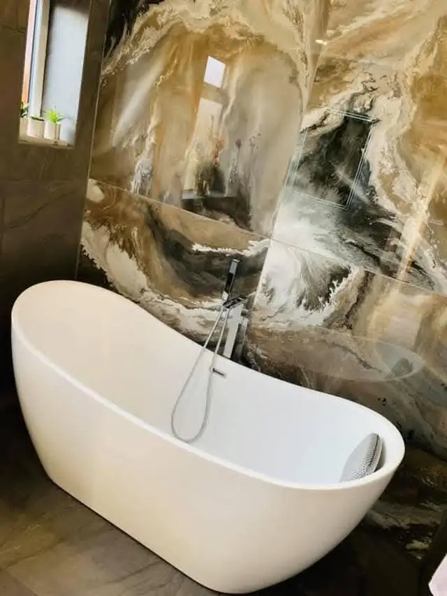 After: a freestanding bath in front of a marble-effect feature wall.
