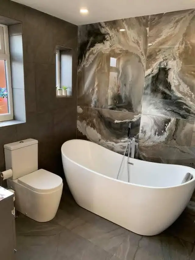 After: the freestanding bath, the feature wall and a new toilet against dark grey tiles.