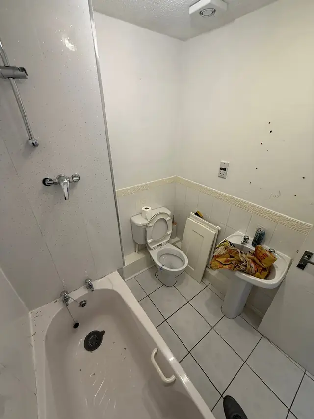 The bathroom before the refit: a bath with an over-bath shower, plain white tiles and a pedestal basin.
