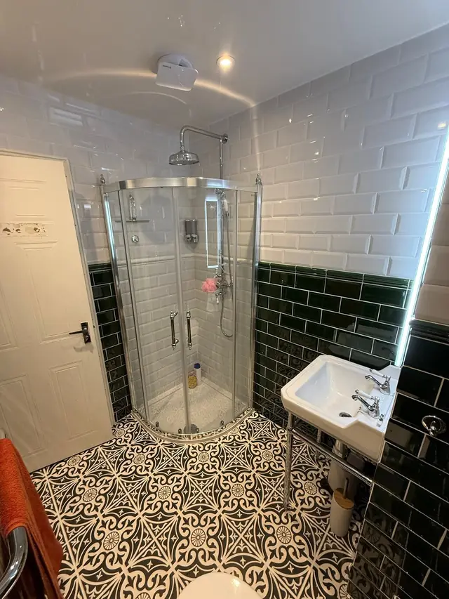 After: the bath replaced by a quadrant shower, with a washstand basin and patterned floor tiles.
