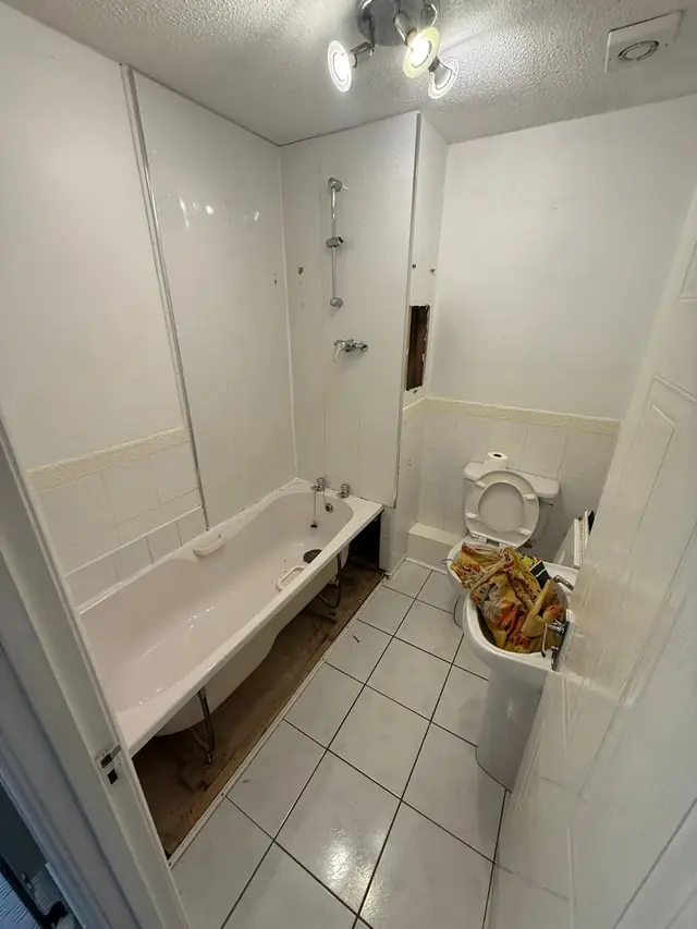 Before: a bath with a shower over it, a toilet and a pedestal basin, with white tiles.
