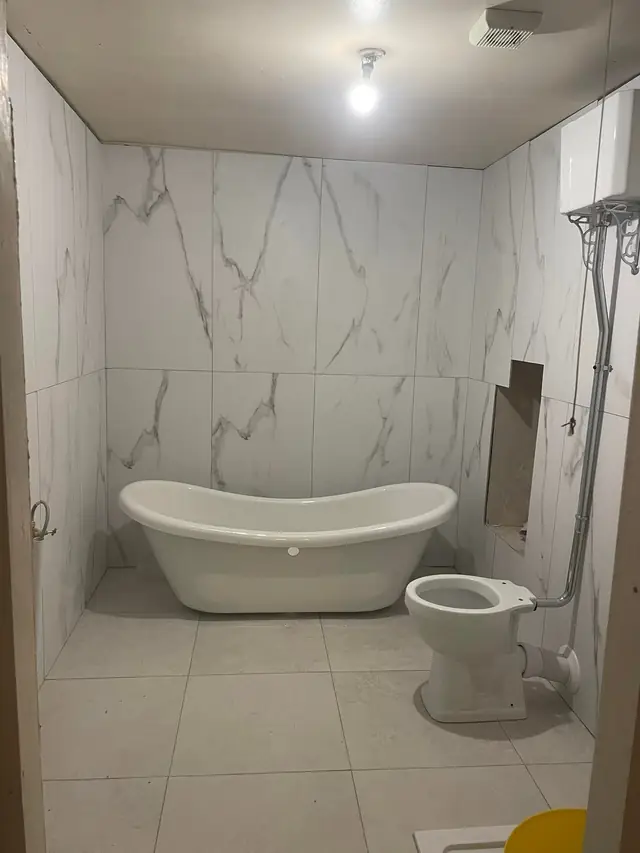 After: a freestanding roll-top bath and toilet against large marble-effect tiles.