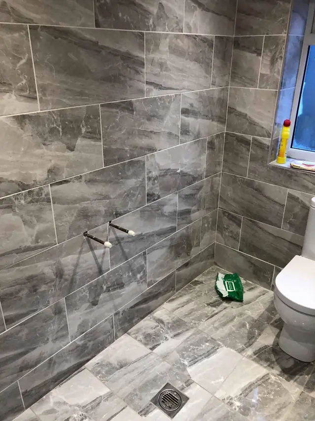 After: the walk-in shower, tiled floor to ceiling in grey stone-effect tiles, with a floor drain.